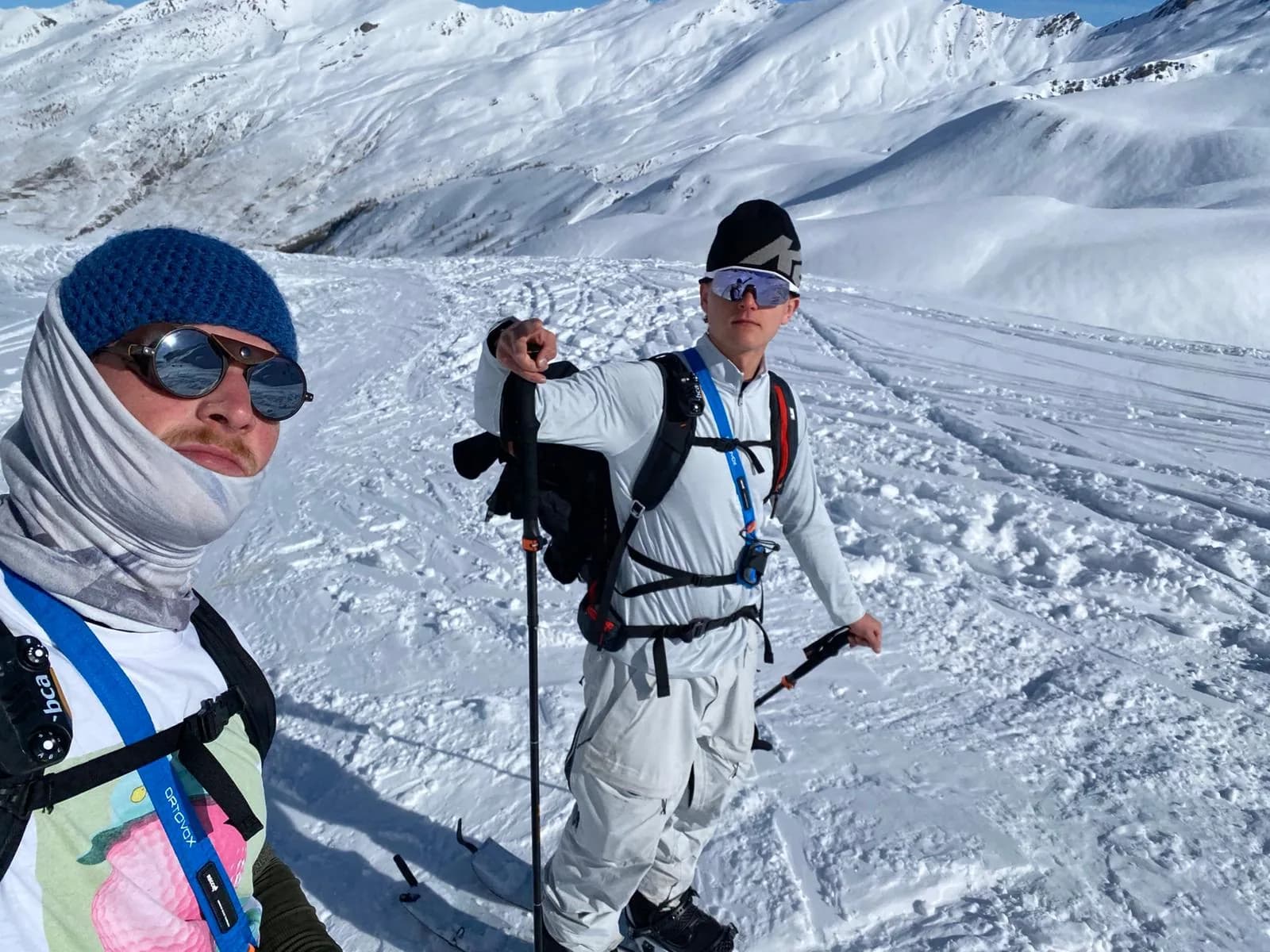 Ziggy, links mit der blauen Mütze und dem LVS-Tragesystem, und Luuk, rechts mit dem Board im Split-Modus und Stöcken, auf einem Schneehang mit Aufstiegsspuren