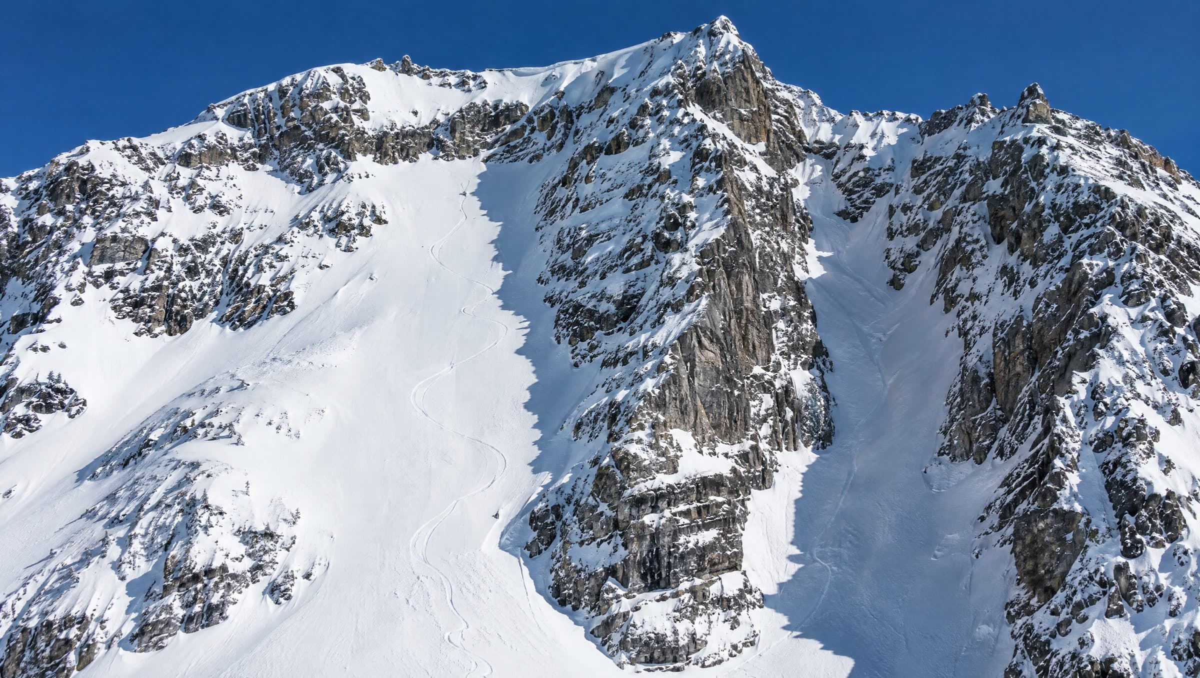 Steile alpine Flanke im Winter mit Felsbändern, einem Couloir und frischen Skispuren